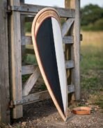 Norman kite shield painted black and white with an engraved knotwork band leaning on a weathered wooden gate