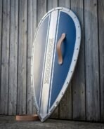 Norman kite shield with blue face, polished steel centre band of knotwork and riveted rim leaning on a wooden wall
