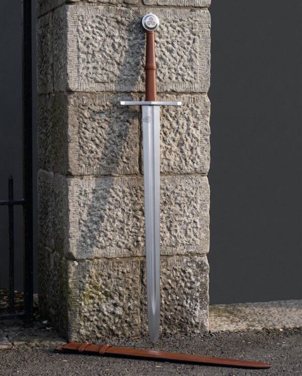 Norman sword standing point down against dressed stone blocks, straight steel crossguard and triple spiral disc pommel above a russet leather grip with a raised riser