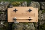 Oak wall plaque with carved Celtic knotwork band and black steel cradles holding a forged axe, propped on a stone wall