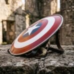Painted round steel shield with polished rim and leather arm straps resting at an angle on weathered stone