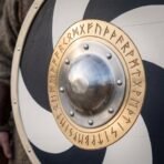 Painted wooden round shield close up of the domed steel boss, riveted rim and engraved brass rune ring