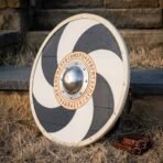 Painted wooden round shield with navy and white pinwheel, steel boss and rune ring leaning on steps in dry grass