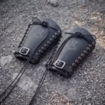 Pair of black leather bracers with engraved Mjolnir, steel eyelet lacing and buckled straps lying on gravel