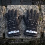 Pair of blackened butted chainmail gauntlets with domed steel studs and white leather buckle straps laid on a weathered stone block outdoors