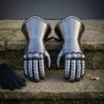 Pair of hand forged steel plate gauntlets with articulated finger lames and Elder Futhark runes cut into the flared cuffs, on mossy stone steps beside a glove.