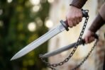 Pair of high carbon steel chain swords with oxblood grips and steel ring pommels held on blackened chains outdoors