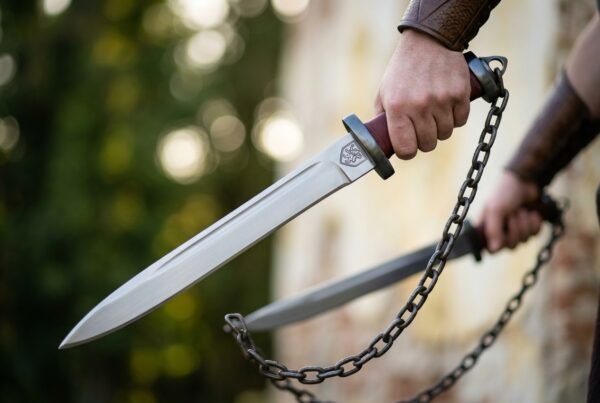 Pair of high carbon steel chain swords with oxblood grips and steel ring pommels held on blackened chains outdoors