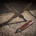 Pair of polished carbon steel spearheads with rune cut sockets crossed on paving stones beside a brown leather cover