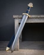 Pattern welded Viking sword leaning on a wooden bench next to its blue leather scabbard with brass chape
