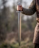 Pattern welded Viking sword with rune cut guard and lobed pommel held point down at the side of a man in a wool tunic