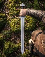 Pattern welded Viking sword with trilobate pommel and rune cut guard held point down against a mossy bank