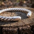 Polished silver finish twisted arm ring with rounded terminals, close up of the rope coil body resting on a cut tree stump