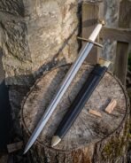 Polished steel arming sword with pale grip and brass fittings leaning on a stump beside its black leather scabbard