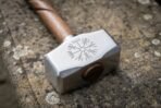 Polished steel blacksmith hammer head engraved with a Vegvisir stave, close up on a lichen covered stone ledge