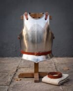 Polished steel breastplate with chased knotwork and rune lettering, red leather straps and belt, front view on a wooden stand