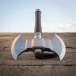 Polished steel double headed axe with twin crescent bits standing upright on paving, viewed straight on against a blue sky