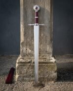 Polished steel knightly sword standing upright against a stone column with red stone pommel and guard stones
