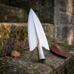 Polished steel spearhead with runed socket upright on worn stone steps beside a brown leather blade cover