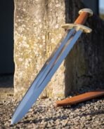 Polished steel Viking sword with brass guard, brass dome pommel and tan leather grip leaning on a stone pillar by its scabbard