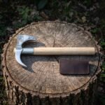 Polished valknut bearded axe with a mirror finished crescent head, hooked horn and pale ash haft lying on a cut tree stump with a dark leather blade cover