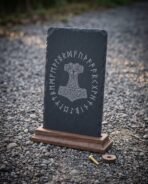 Riven slate plaque engraved with Mjolnir and a ring of Elder Futhark runes standing on its walnut base on gravel