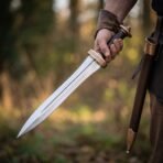 Roman pugio dagger with double edged midrib blade, engraved bronze guard and dark grip held beside its leather sheath