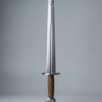 Rondel dagger trainer with two steel discs, a riveted blunting plate over the point and a fluted walnut grip lying on a plain grey studio backdrop