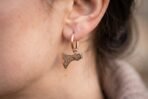 Rose gold tone Viking axe hoop earring with Celtic knot head worn on the ear, shown close up against soft brown hair