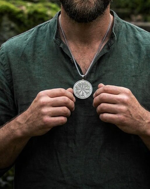 Round helm of awe pendant on a steel box chain held in both hands by a bearded man wearing a green linen shirt