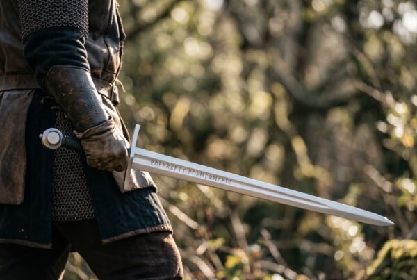 Rune engraved Viking sword with straight cross guard held point forward by a man in mail in the woods