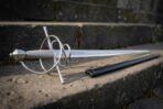 Rune etched rapier with swept steel hilt and wire wrapped grip resting on stone steps beside its black scabbard