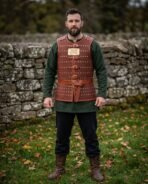 Russet leather cuirass with brass domed rivets, buckle straps and brass chest plaque worn by a man standing by a stone wall