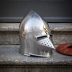 Satin steel pig faced bascinet with pierced hounskull visor, etched knotwork brow band and brass hinges, three quarter view on a stone step