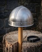 Satin steel Viking helmet with a crown strip and riveted brow band on a wooden post in front of dark stone
