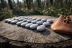 Set of white engraved rune stones spread across a tree stump beside a tan leather drawstring pouch in a forest