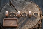 Seven piece viking beard beads set of bronze tone Valknut stamped bands and twisted wire rings arranged on a cracked oak log slice beside a small walnut tray