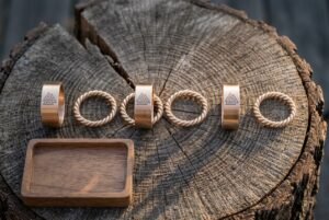 Seven piece viking beard beads set of bronze tone Valknut stamped bands and twisted wire rings arranged on a cracked oak log slice beside a small walnut tray