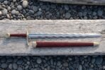Side ring flamberge sword with a polished undulating wave blade, brass crossguard and side ring, red leather grip, Celtic knot wheel pommel and brass mounted scabbard