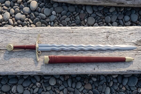 Side ring flamberge sword with a polished undulating wave blade, brass crossguard and side ring, red leather grip, Celtic knot wheel pommel and brass mounted scabbard
