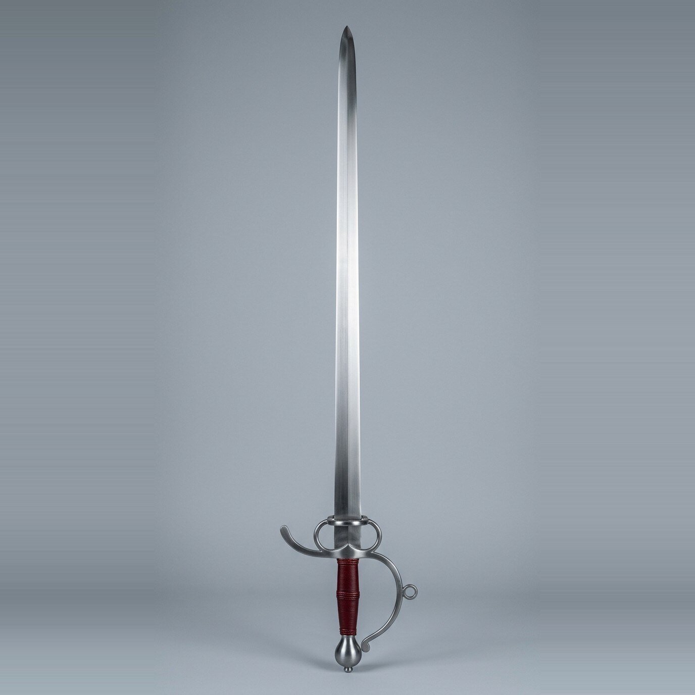 Skelvard sidesword trainer Sidesword trainer with two finger rings, a knuckle bow ending in a free scroll, side ring and oxblood leather grip standing point up against a plain grey studio backdrop