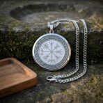 Close up of a silver finish vegvisir pendant with knotwork border, curb chain and lobster clasp laid on a mossy stone ledge