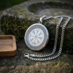 Silver finish vegvisir pendant with knotwork border and curb chain propped against a mossy stone basin, wooden tray beside