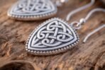 Silver tone Celtic knotwork earrings with shield shaped drops and beaded borders, close up on rough wood