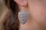 Silver tone Celtic knotwork shield earring with hook wire worn on an ear, side view