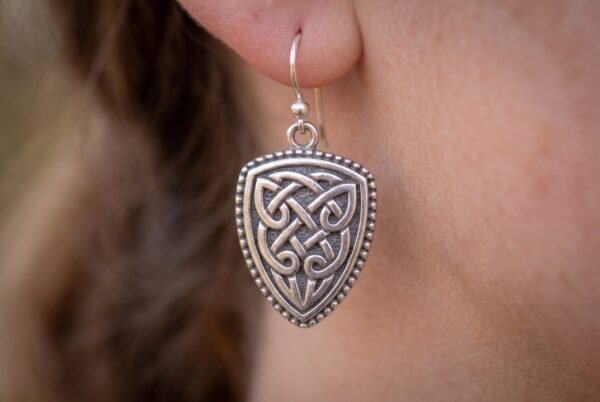 Silver tone Celtic knotwork shield earring with hook wire worn on an ear, side view