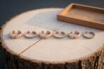 Six bronze tone adjustable rings, valknut stamped bands and twisted cuffs, lined up on a pale sawn log with an oak tray behind