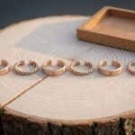Six piece viking ring set of open ended bronze tone Valknut bands and twisted wire cuffs laid across a pale birch log slice beside a shallow wooden tray