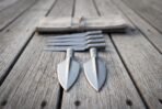 Socketed spearheads stacked on grey decking, two broad leaf heads in front and four narrow heads behind a canvas roll