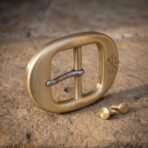 Solid brass oval belt buckle with an engraved vegvisir and steel tongue standing on sandstone with two brass screw studs